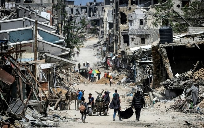 Palestinos caminham entre edifícios destruídos em Khan Yunis, sul da Faixa de Gaza, em 23 de abril de 2024