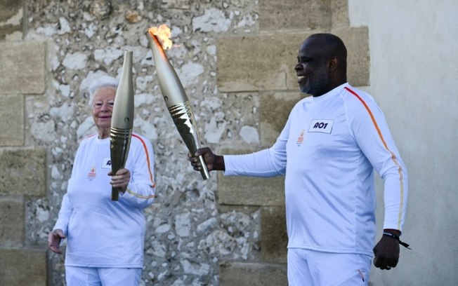 O ex-jogador de futebol Basile Boli (à direita) entrega a tocha olímpica a Colette Cataldo (à esquerda), torcedora símbolo do Olympique de Marselha, no primeiro revezamento da chama olímpica, em Marselha, França, em 9 de maio de 2024