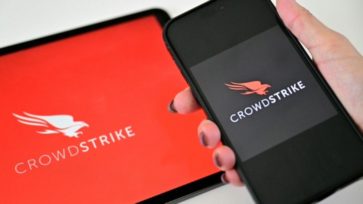 Mulher segura um telefone perto de um tablet que exibe o logotipo da empresa de segurança cibernética CrowdStrike, em 19 de julho de 2024, em Dubai, nos Emirados Árabes Unidos