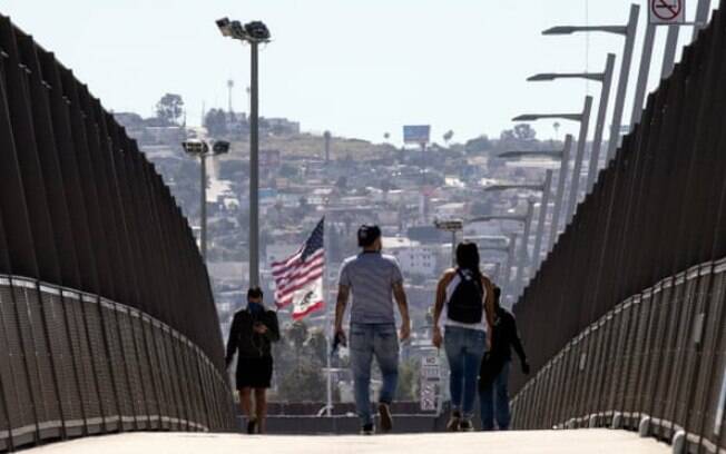 Pessoas usando máscaras cruzam a ponte sobre a rodovia na fronteira EUA-México em San Diego, Califórnia