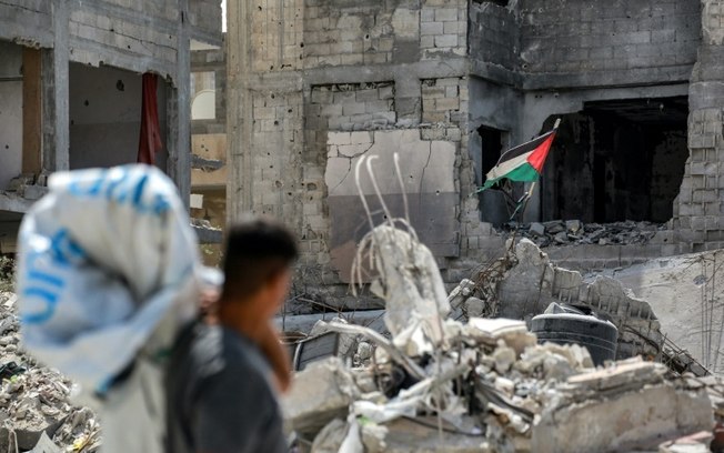 Um homem olha para uma bandeira palestina rasgada hasteada em um prédio em ruínas na cidade de Khan Younis, Faixa de Gaza, em 16 de setembro de 2024.