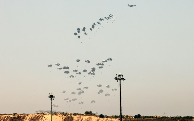 Foto tirada da fronteira sul de Israel com a Faixa de Gaza mostra um avião militar lançando paraquedas de ajuda humanitária sobre o território palestino sitiado em 4 de abril de 2024