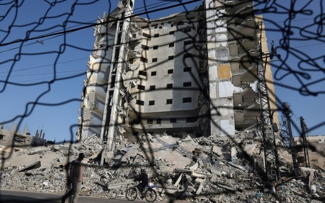 Palestino caminha diante dos escombros de prédios destruídos por bombardeios israelenses em Rafah, sul da Faixa de Gaza