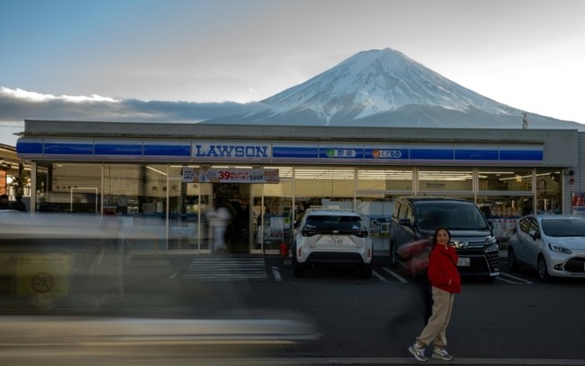 Turista posa diante de loja de conveniência com vista para o Monte Fuji, na cidade japonesa de Fujikawaguchiko, em 1º de janeiro de 2024