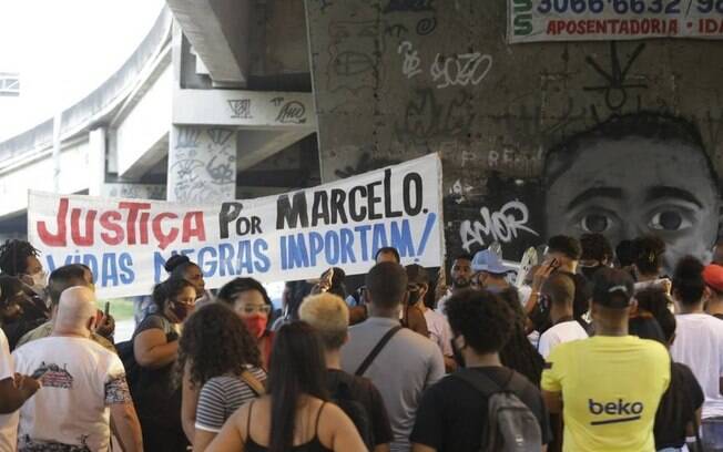 Faixa pede justiça por Marcelo. Ao fundo, grafite feito em sua homenagem, no local da tragédia 