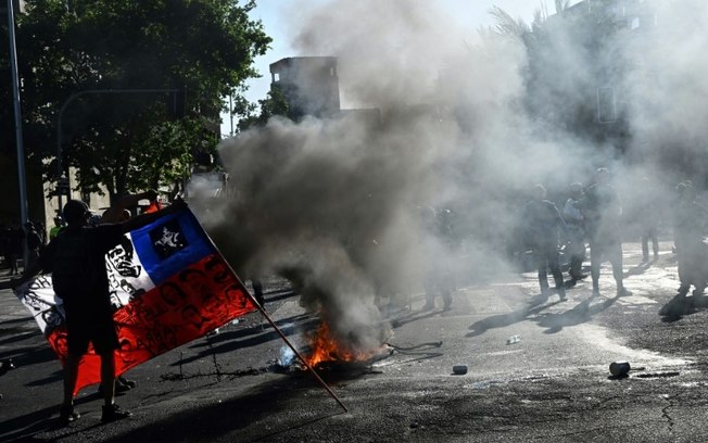 Manifestante segura a bandeira do Chile perto de uma barricada durante a marcha pelo quinto aniversário da 