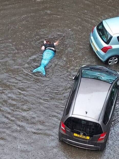 mulher vestida de sereia nadando em área alagada na rua