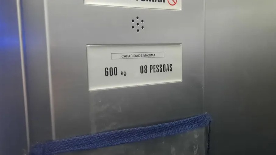 Aviso informa capacidade de 8 pessoas em elevador onde 11 passageiros entraram