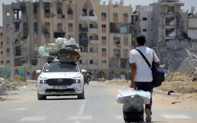 Palestinos que fugiram de Rafah, no sul de Gaza, carregam seus pertences em cima de um caro enquanto um homem puxa sua mala ao chegarem para se abrigarem em Khan Yunis, em 12 de maio de 2024