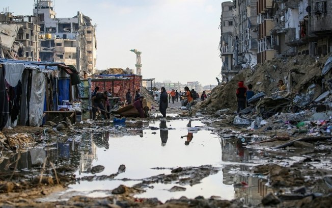 Palestinos deslocados caminham entre os escombros de prédios em Khan Yunis