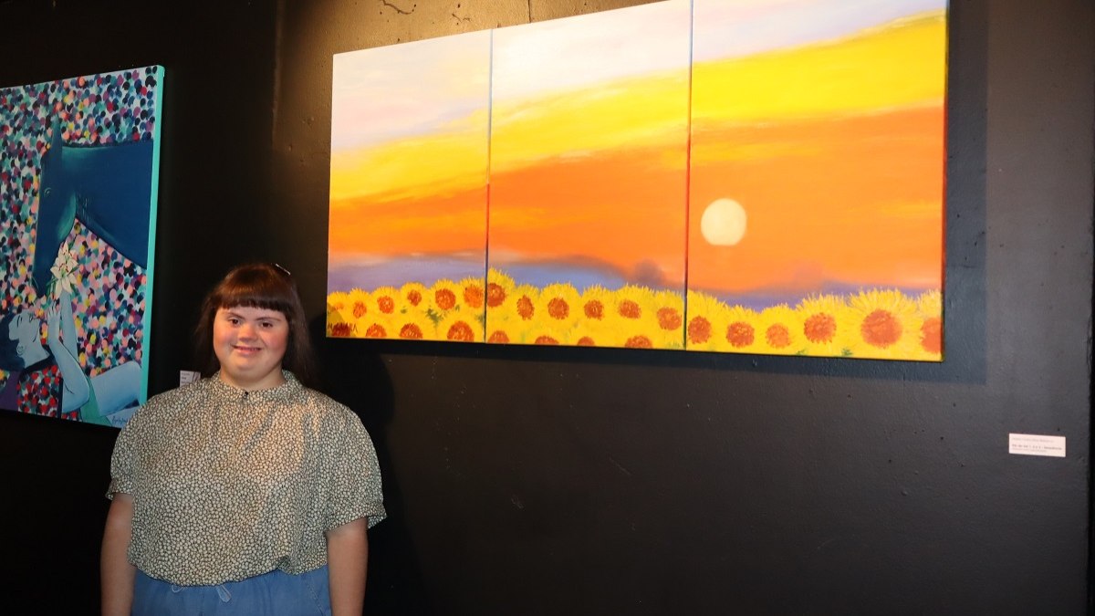 Artista Maria Clara Dias Rebeca ao lado de suas obras durante exposição no Coletiva Vinhedo