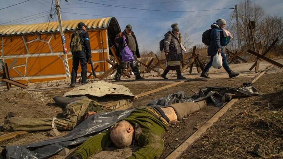 Civis ucranianos passam pelos corpos de dois soldados russos entre as cidades de Irpin e Bucha, perto de Kiev