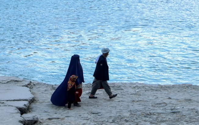 Um homem afegão, uma mulher vestida de burca e uma criança caminham nas margens do rio Kokcha em Fayzabad, em 14 de fevereiro de 2024