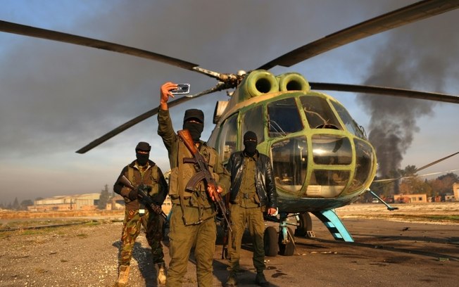 Combatentes contrários ao regime posam para fotografia ao lado do helicóptero do Exército em 2 de dezembro de 2024 no aeroporto militar de Nayrab, na cidade síria de Aleppo