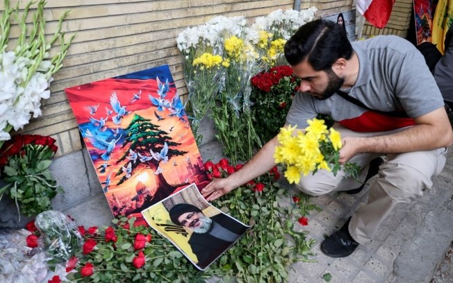 Um homem coloca um retrato do chefe do Hezbollah, Hassan Nasrallah, e flores no local de um memorial montado do lado de fora da embaixada do Líbano em Teerã, em 18 de setembro de 2024