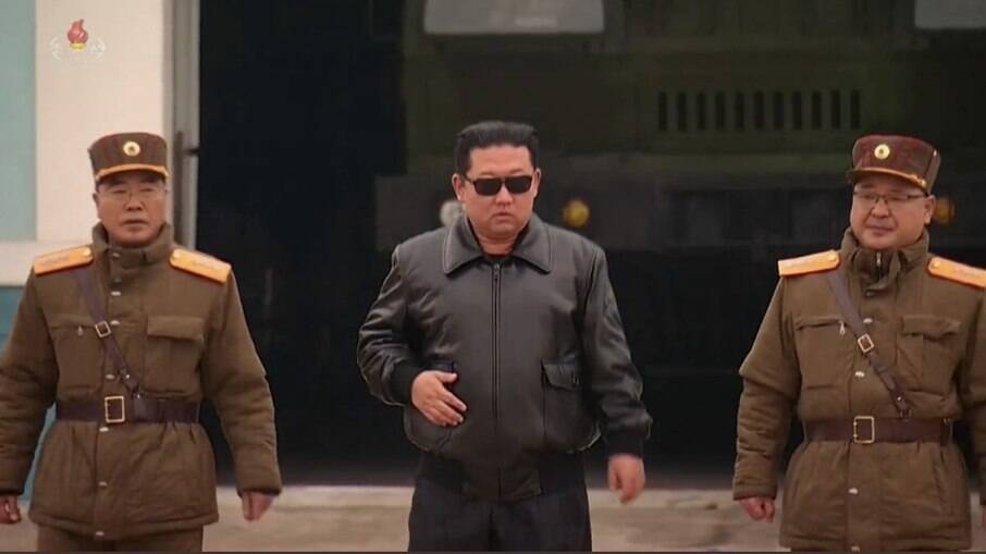 Ditador Kim Jong-un de jaqueta de couro e óculos escuros de estilo aviador andando no meio de dois militares