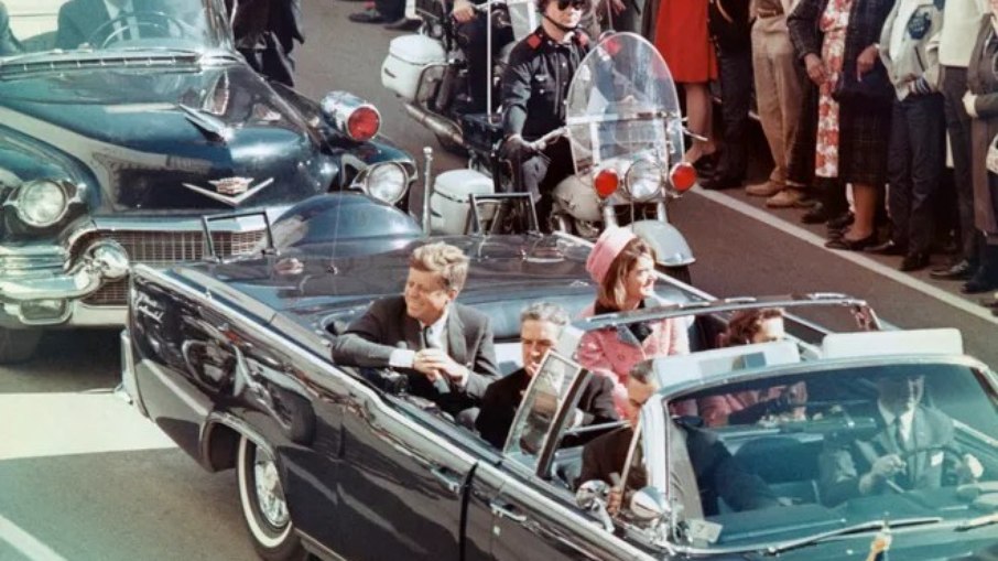 O presidente John F. Kennedy minutos antes de ser assassinado, quando seu carro passava pela Dealey Plaza. O presidente John F. Kennedy minutos antes de ser assassinado, quando seu carro passava pela Dealey Plaza.