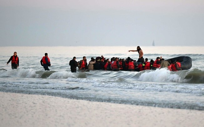 Barqueiro (C) é flagrado de pé em meio a migrantes a bordo de um bote de borracha antes de iniciar a travessia ilegal do Canal da Mancha rumo ao Reino Unido, próximo a Gavlines, no norte da França, em 11 de julho de 2022