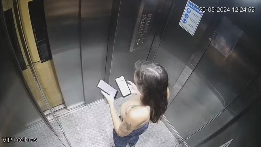 Júlia Andrade com dois telefones no elevador do prédio