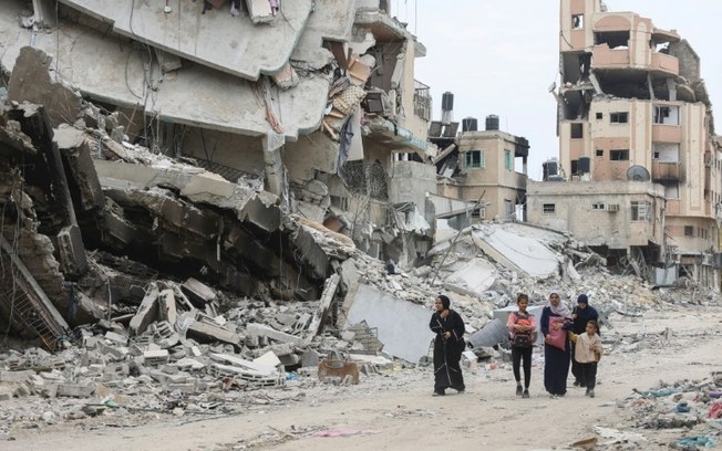 Mulheres e crianças palestinas passam em meio a ruínas de edifícios destruídos por um bombardeio de Israel na cidade de Gaza, em 8 de abril de 2024