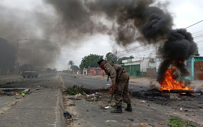 Forças de segurança moçambicanas se posicionam perto de uma barricada incendiária em Maputo, 24 de dezembro de 2024