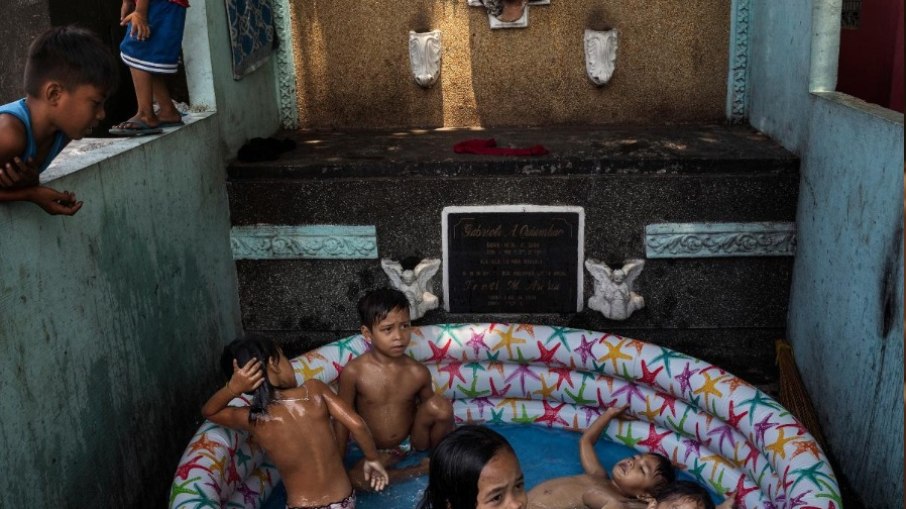 Crianças em piscina ao lado de túmulo