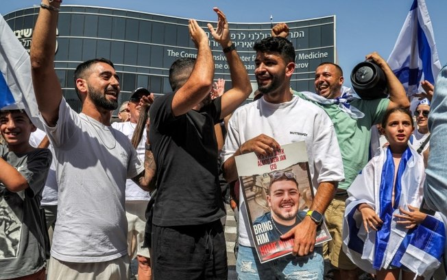 Homem segura um cartaz com o rosto de Almog Meir Khan, um dos quatro israelenses resgatados de Gaza, em Ramat Gan, em 8 de junho de 2024