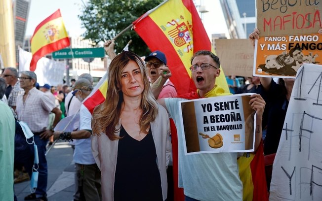 Um homem envolto na bandeira espanhola grita ao lado de uma reprodução de uma imagem de Begoña Gómez, esposa do primeiro-ministro espanhol, Pedro Sánchez, do lado de fora do tribunal de Madri, onde ela compareceu em 5 de julho de 2024