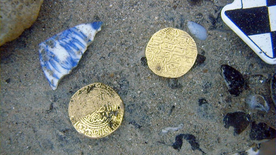 Os artefatos recuperados no local do naufrágio incluem moedas de ouro com inscrições em árabe Os artefatos recuperados no local do naufrágio incluem moedas de ouro com inscrições em árabe