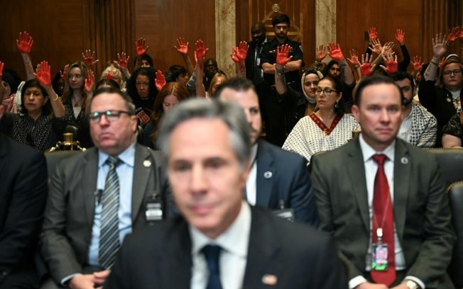 Manifestantes pró-palestinos levantam as mãos pintadas em sinal de protesto enquanto o secretário de Estado dos Estados Unidos, Antony Blinken, se pronuncia no Senado Manifestantes pró-palestinos levantam as mãos pintadas em sinal de protesto enquanto o secretário de Estado dos Estados Unidos, Antony Blinken, se pronuncia no Senado