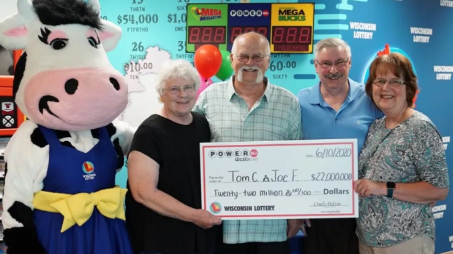 Tom Cook e Joseph Feeney posam com suas esposas segurando um cheque representando o prêmio no valor de 22 milhões de dólares Tom Cook e Joseph Feeney posam com suas esposas segurando um cheque representando o prêmio no valor de 22 milhões de dólares