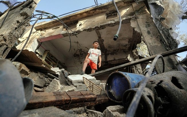 Jovem palestino diante de casa destruída por bombardeio israelense em Nuseirat, na Faixa de Gaza, em 23 de maio de 2024