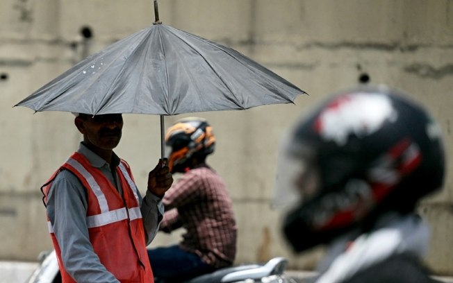 Enquanto os países em desenvolvimento pedem aumentos na ajuda climática, um funcionário de uma cabine de pedágio se protege sob um guarda-chuva durante uma onda de calor recorde em Nova Délhi
