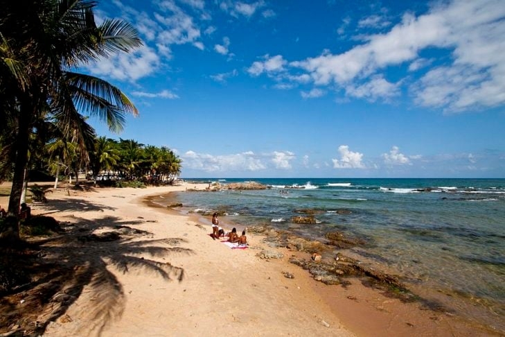 Um exemplo é a Praia de Itapuã, conhecida pelas suas areias douradas, coqueiros e águas tranquilas. O local já foi até mencionado em uma música música de Vinicius de Moraes e Dorival Caymmi. Reprodução: Flipar