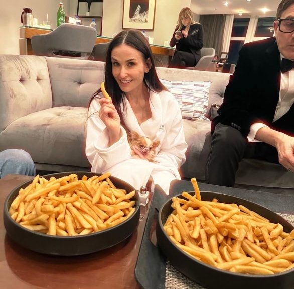 Em uma foto postada por sua filha, Moore aparece sentada no chão de roupão, com seu cachorro no colo e com duas tigelas cheias de batata frita ao lado.  Reprodução: Flipar