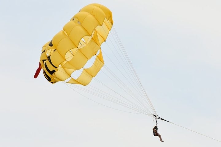 Conforme o barco acelera, o parasail é inflado pelo vento, elevando o participante a alturas que podem variar entre 30 e 150 metros, dependendo das condições climáticas e do comprimento da corda. Reprodução: Flipar