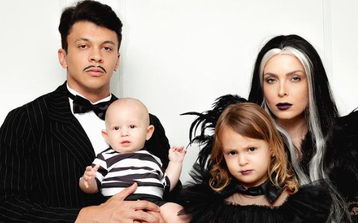 Julio Cocielo, Tata Estanieck e Bia Cocielo vestidos de Família Addams para o mêsversário de 5 meses de Caio Cocielo  Reprodução/Instagram