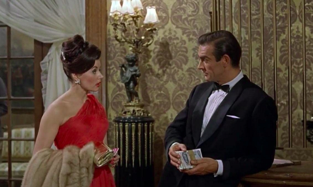 Coube à atriz Eunice Gayson a função de primeira Bond Girl da história. Ela também teve a sorte de ser a primeira agraciada com o clássico bordão “Bond… James Bond”, ao perguntar o nome do herói. Reprodução: Flipar