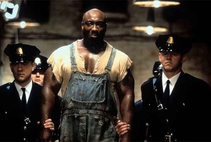 À Espera de um Milagre (1999): dirigido por Frank Darabont, é um drama baseado na obra de Stephen King que se passa na década de 1930 em uma prisão. A história segue Paul Edgecomb (Tom Hanks), um guarda do corredor da morte, que se depara com John Coffey (Michael Clarke Duncan), um prisioneiro condenado por um crime horrendo. No entanto, Coffey revela ter habilidades sobrenaturais e uma natureza gentil, desafiando as percepções de Edgecomb sobre justiça e humanidade. Reprodução: Flipar