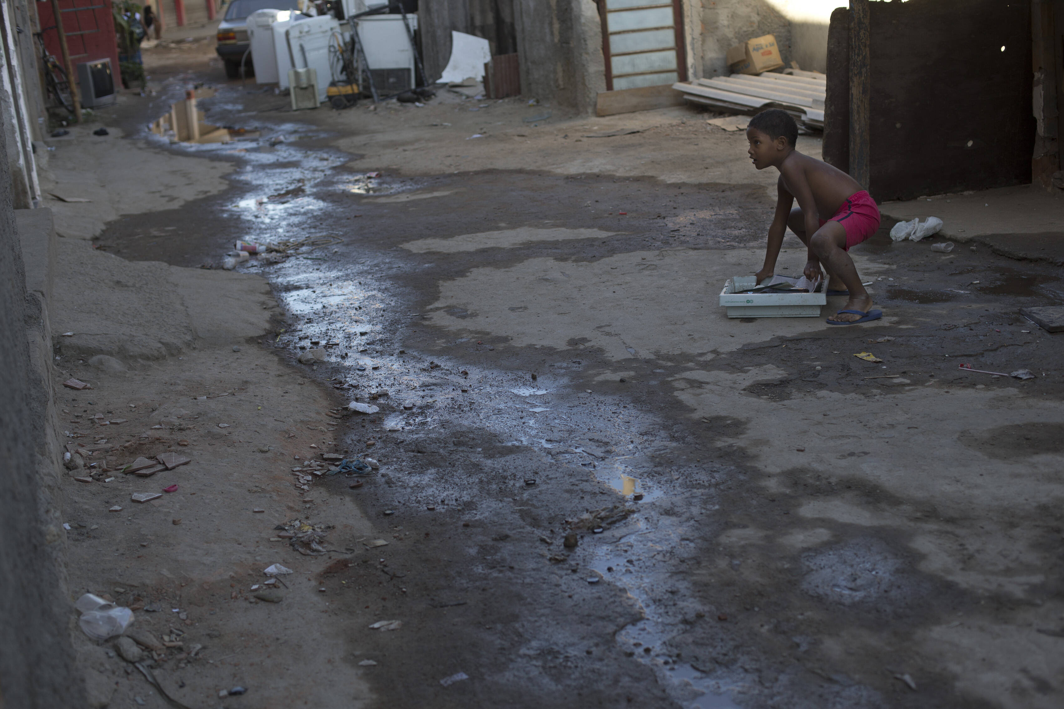 Complexo da Maré é envolvido por áreas de água poluída. Criança brinca em rua com esgoto a céu aberto. Foto: Silvia Izquierdo/AP