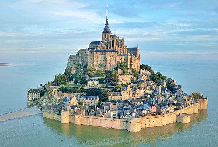 MONTE SAINT-MICHEL - É uma ilha rochosa, cerca por muralhas, na região da Normandia, na França. No decorrer da Guerra dos Cem anos foi uma defesa impenetrável, pois todas as tentativas inglesas de tomá-la foram fracassadas. Assim, virou um símbolo do nacionalismo francês e foi utilizada como prisão durante a Revolução Francesa. Reprodução: Flipar