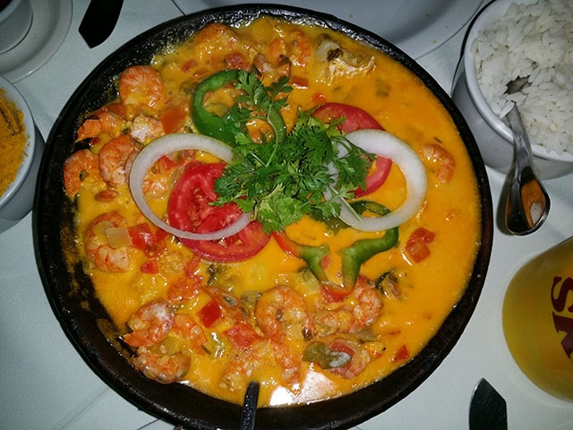 Moqueca baiana: Um prato de peixe cozido com azeite de dendê, leite de coco, cebola, tomate e pimentão, cheio de sabores marcantes. Geralmente servido com pirão e arroz. Calorias: cerca de 170 kcal. Reprodução: Flipar