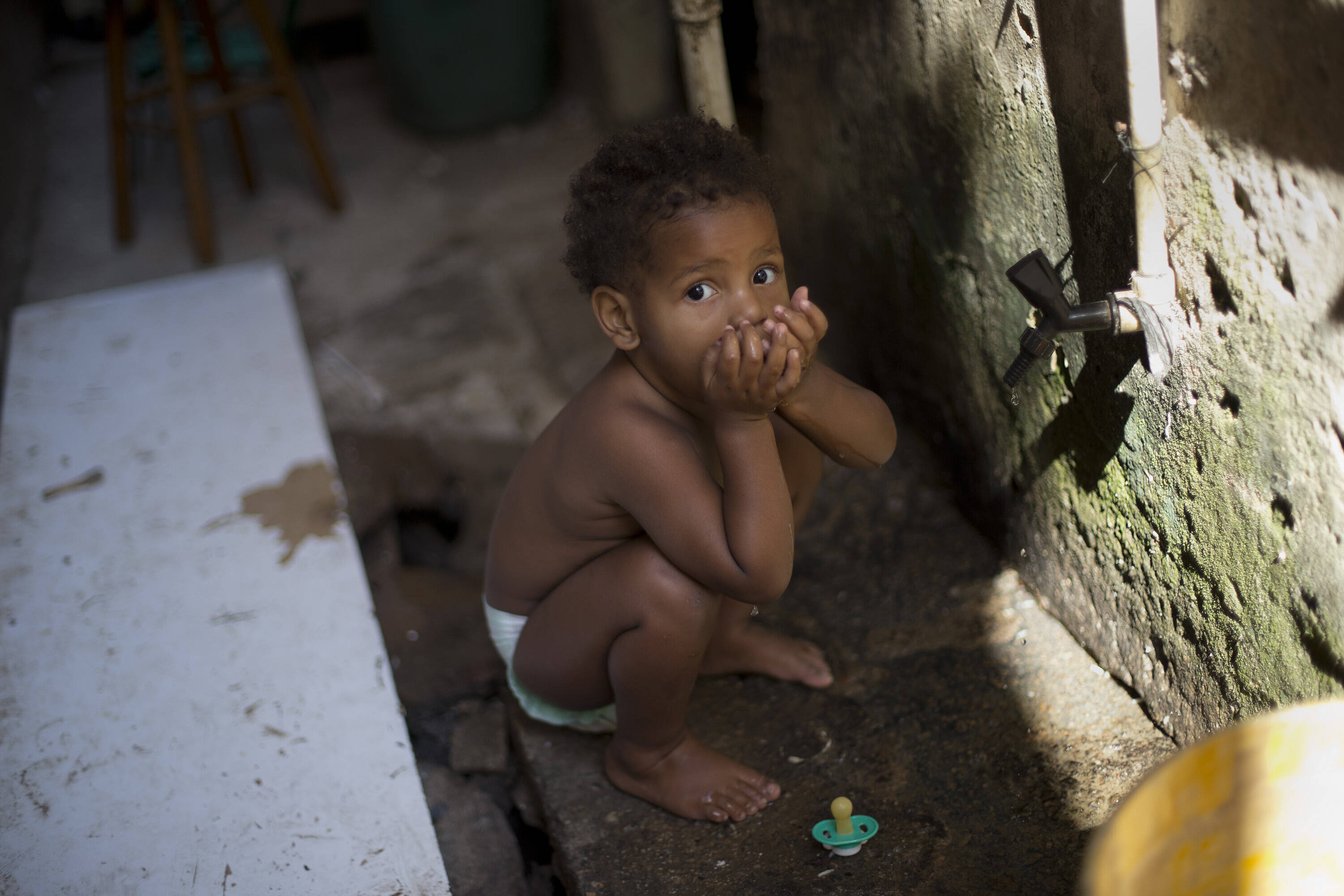 Criança bebe água filtrada em tanque próprio na sua casa na favela Mandela no Rio. Foto: Silvia Izquierdo/AP