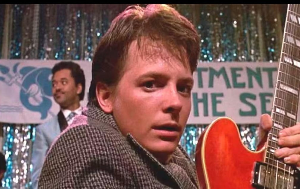 No filme lançado em 1985, que abriu a série da franquia, o adolescente Marty McFly (J.Fox)  volta ao passado numa experiência de viagem no tempo. E toca guitarra durante um evento. Reprodução: Flipar