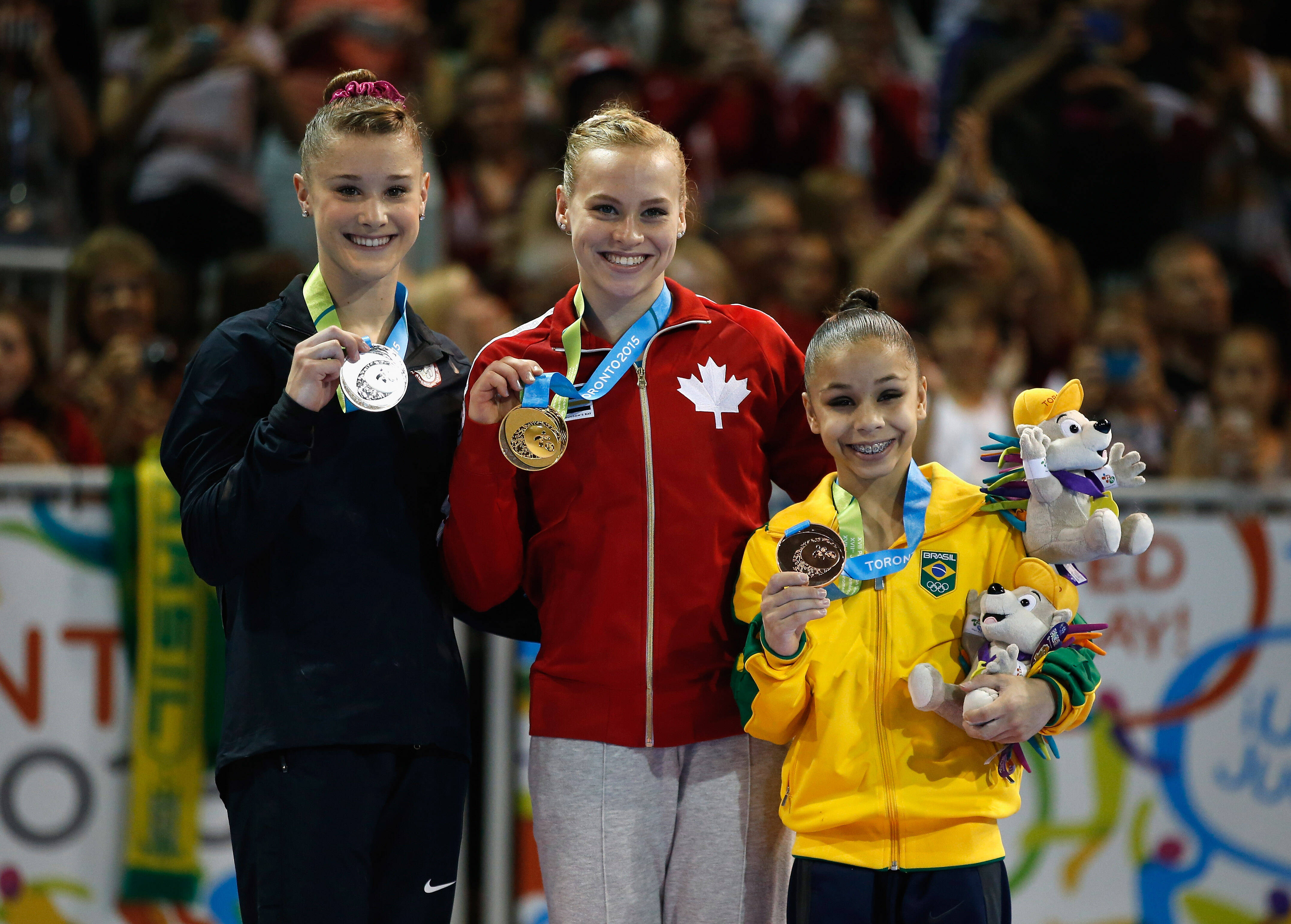 A pequenina Flavia Saraiva ao lado da medalhista de ouro Ellie Black e da medalhista de prata Madison Desch, no individual geral  Ezra Shaw/Getty Images