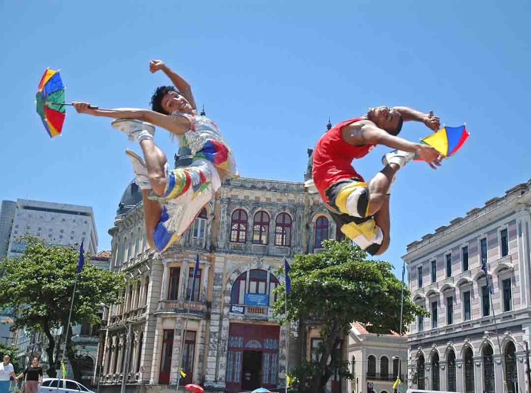 As sombrinhas coloridas assumem um papel importante na dança. Elas auxiliam na coreografia, ajudando os dançarinos a obter equilíbrio ao executar passos acrobáticos. Além disso, trazem um colorido especial à dança.  Reprodução: Flipar