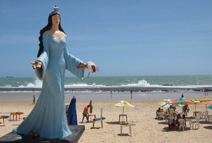 A imagem de Iemanjá varia conforme as tradições locais, mas geralmente é representada como uma mulher majestosa, muitas vezes vestida em tons de azul e branco, segurando símbolos como conchas e peixes.  Reprodução: Flipar