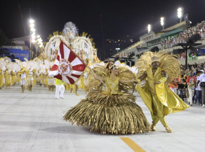 A porta-bandeira carrega consigo toda a ancestralidade da formação negra do samba e quando gira emana o axé de seu pavilhão. Ela conduz e apresenta o pavilhão, que deve estar sempre aberto no momento do giro. Também tem status e postura de rainha dentro de uma escola de samba, com gestos elegantes, suaves e leves. Reprodução: Flipar