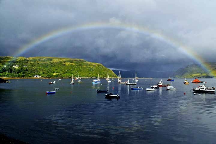 Ilha de Skye - Cidade: Escócia-  O clima frequentemente chuvoso e a luz solar intermitente criam condições ideais para a formação de arco-íris sobre as paisagens montanhosas e dramáticas da Ilha de Skye, tornando-a famosa pelos arcos vibrantes que contrastam com o céu nublado.
 Reprodução: Flipar