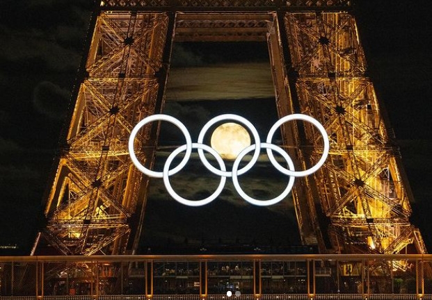 A foto em questão foi um registro impressionante feito pelo fotógrafo Greg Martin, que mostra o momento exato em que a Lua aparece no centro de um dos arcos olímpicos.  Reprodução: Flipar